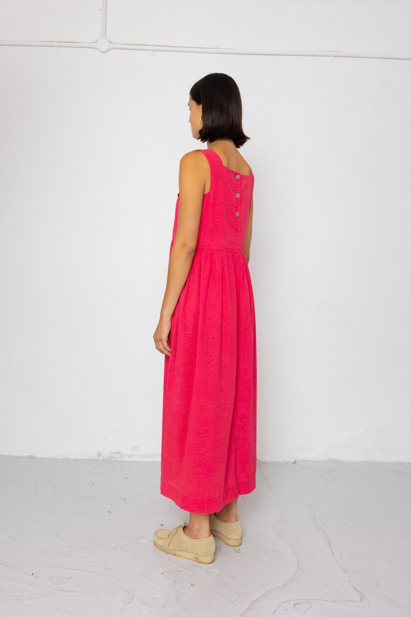 Woman wearing a pink dress with buttons on the back against a white background