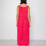 Person wearing a pink dress with buttons on the back against a white background