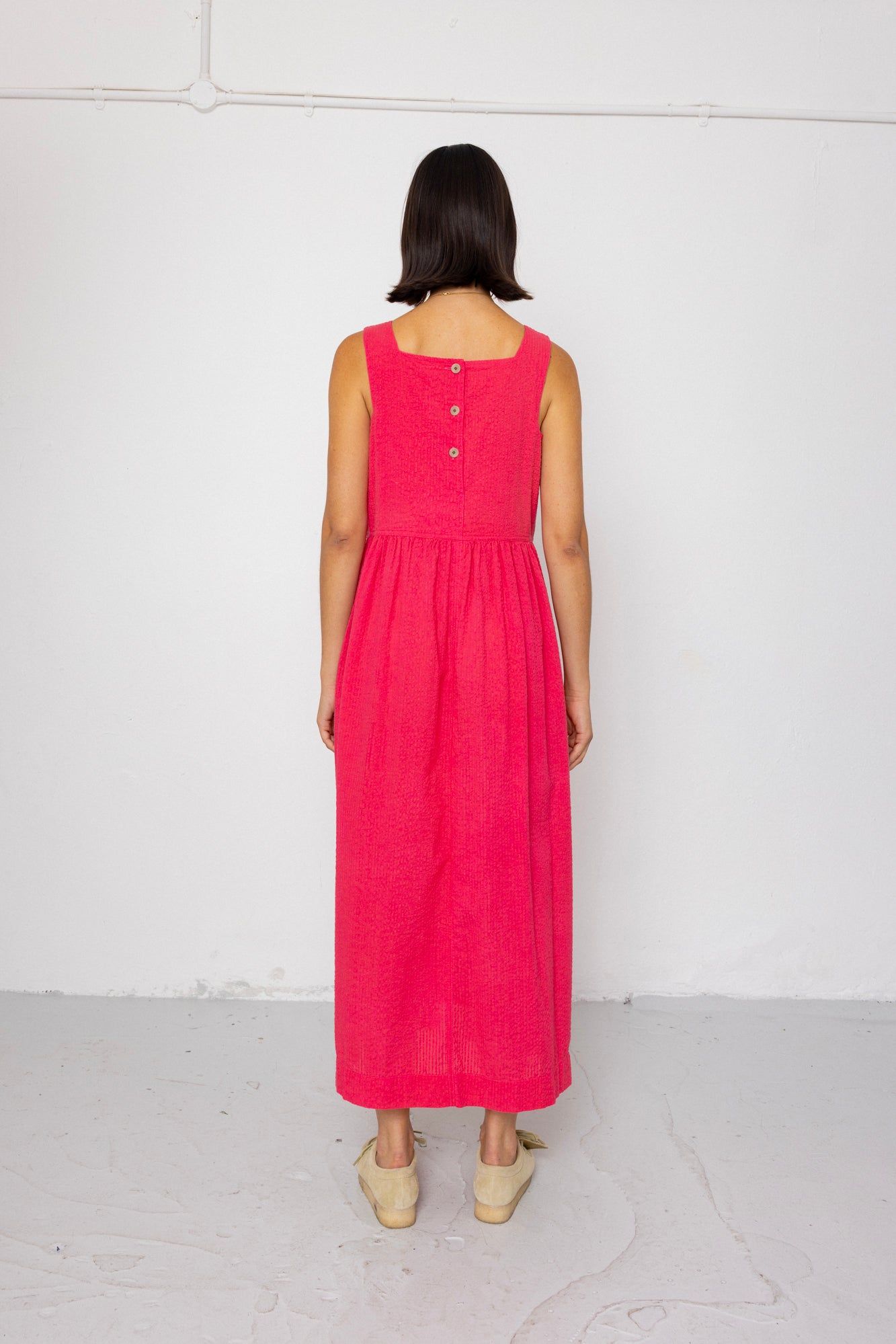 Person wearing a pink dress with buttons on the back against a white background