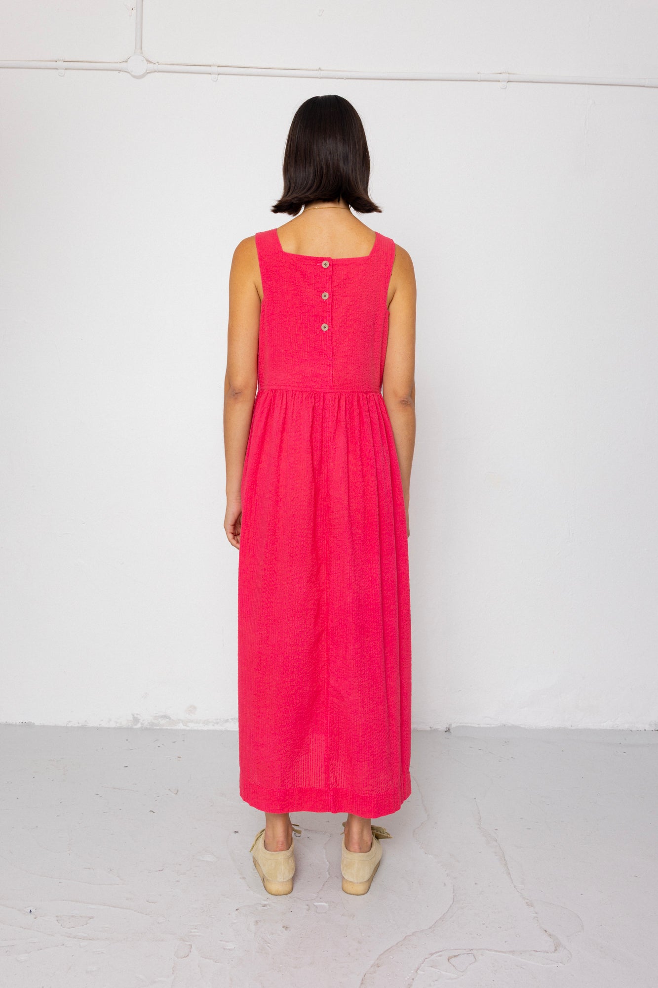 Person wearing a pink dress with buttons on a white background