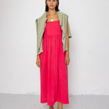 Woman wearing a pink dress with a green jumper over her shoulders on a white background