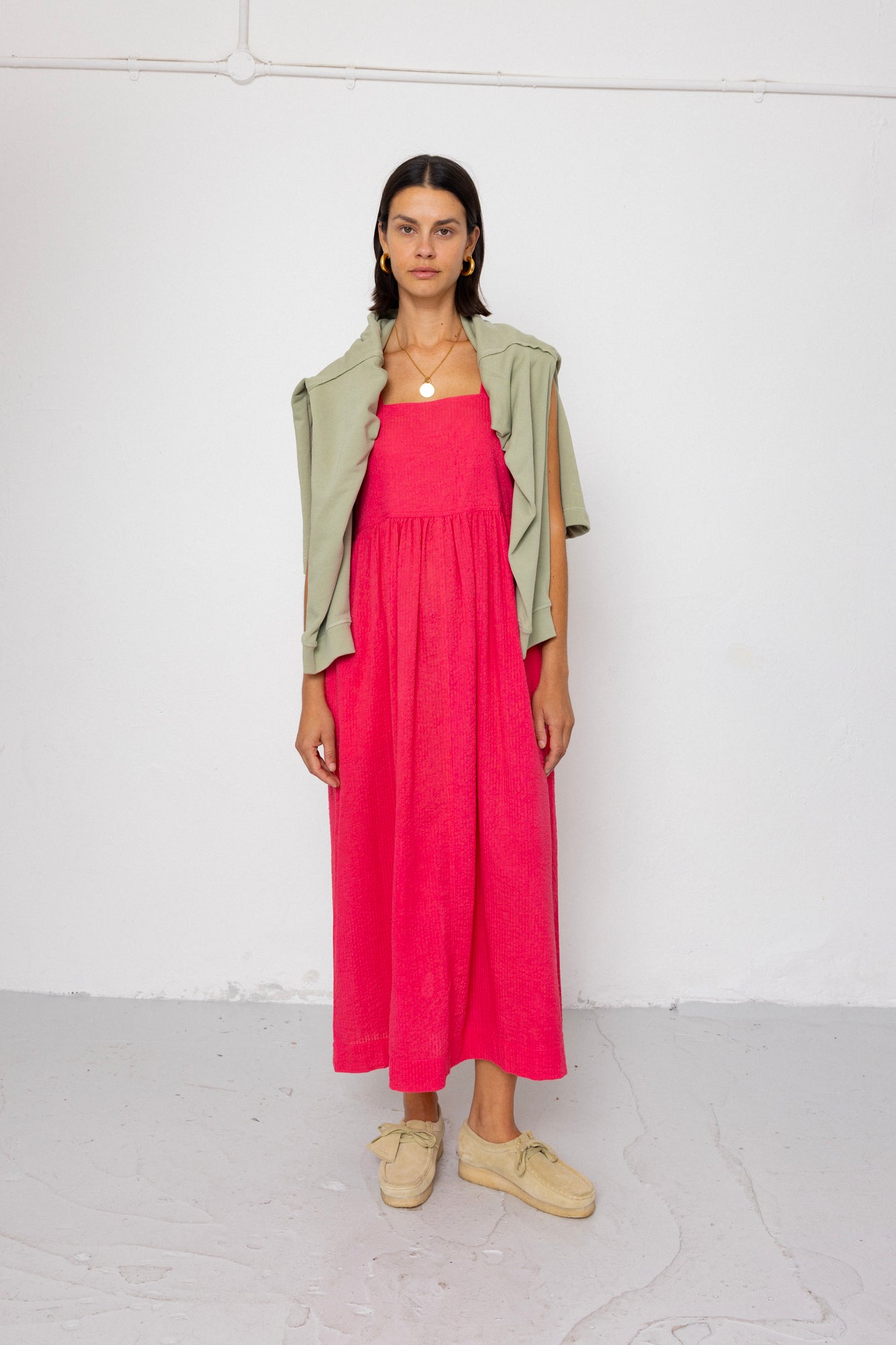 Woman wearing a pink dress with a green jumper over her shoulders on a white background