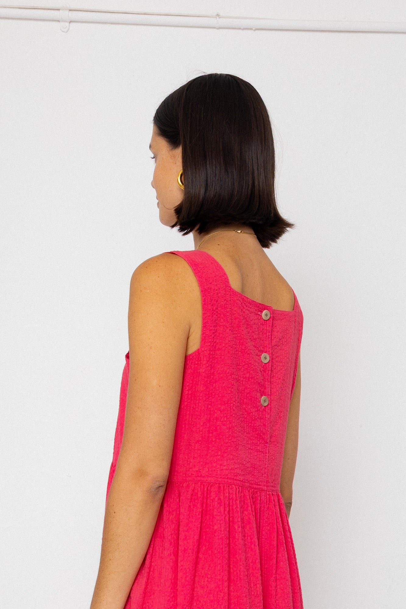 Woman wearing a pink dress with buttons on a white background