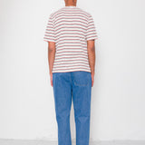 Person wearing a striped shirt and blue jeans standing against a white wall.