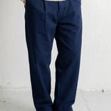 A person wearing navy blue relaxed-fit trousers, a cream and navy striped long-sleeve shirt, and navy canvas sneakers, standing against a white textured wall.