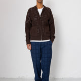 Man wearing a brown cardigan, white shirt, blue checkered pants, and gray shoes against a white background