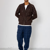 Man wearing a brown patterned sweater and blue pants against a white background