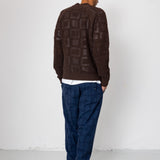 Person wearing a brown patterned sweater and blue pants against a white background