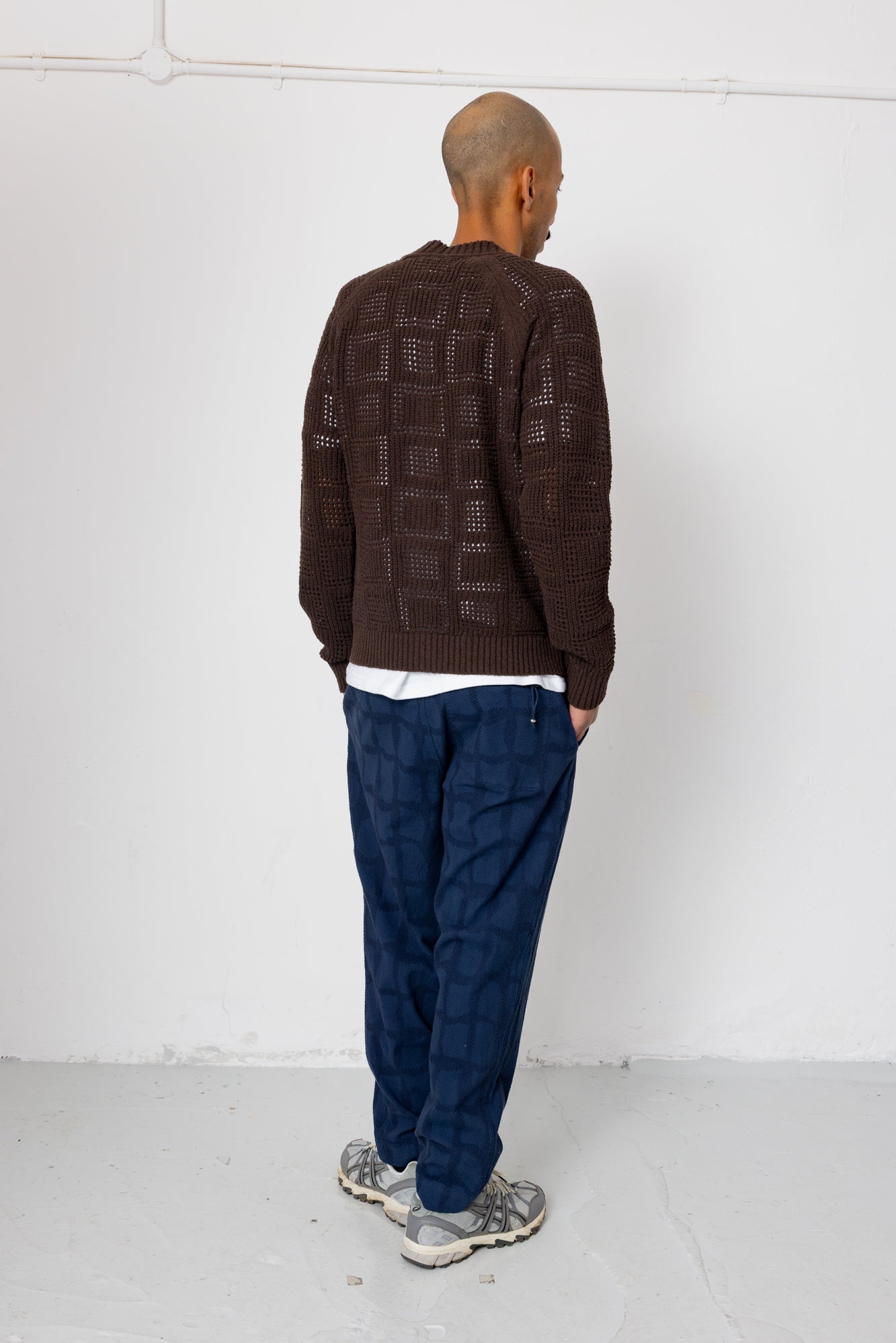 Person wearing a brown patterned sweater and blue pants against a white background