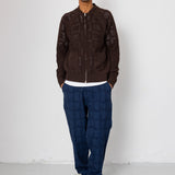 Man wearing a brown jacket and blue pants standing against a white background