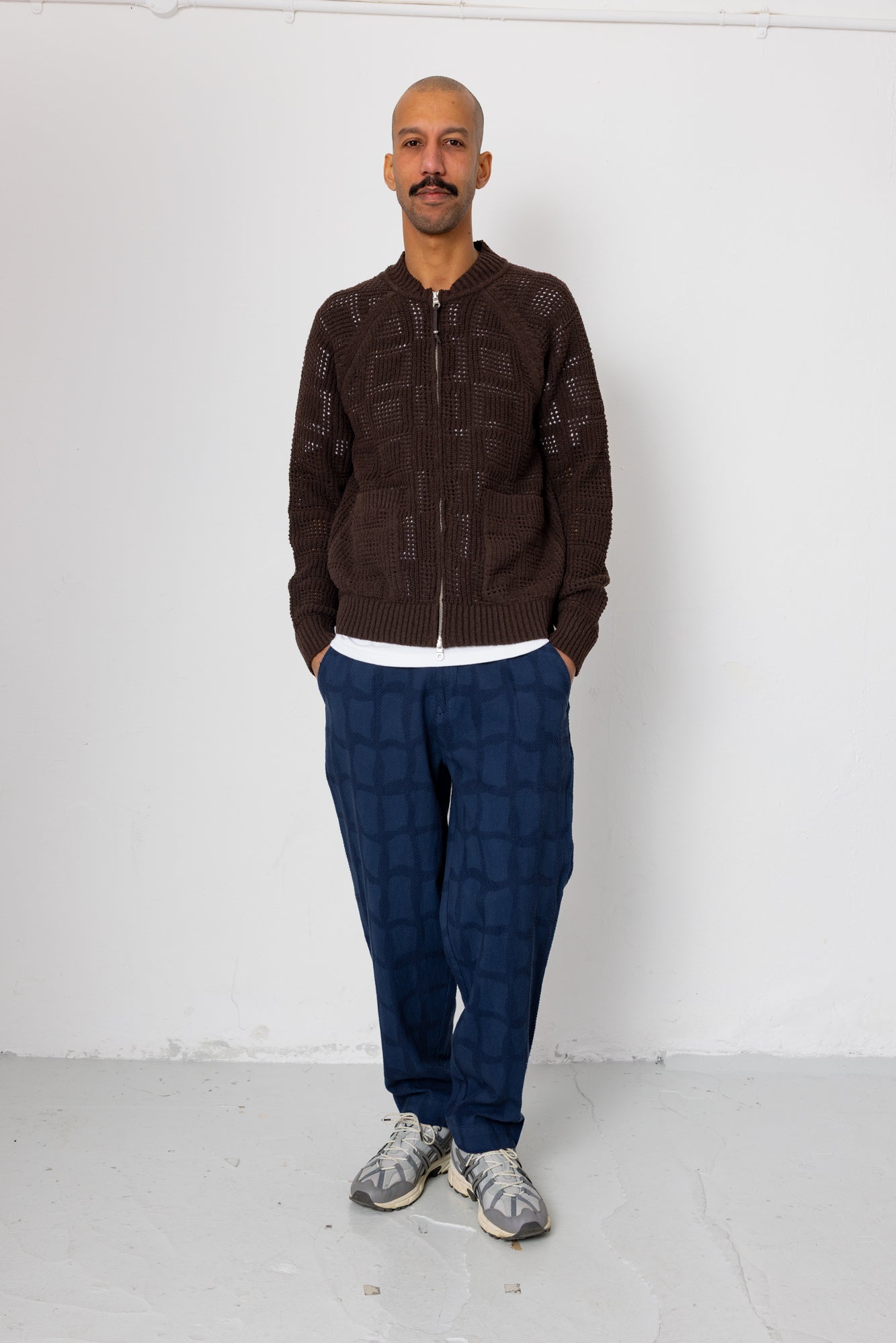Man wearing a brown jacket and blue pants standing against a white background