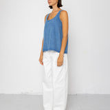 Woman wearing a blue tank top and white pants against a white background