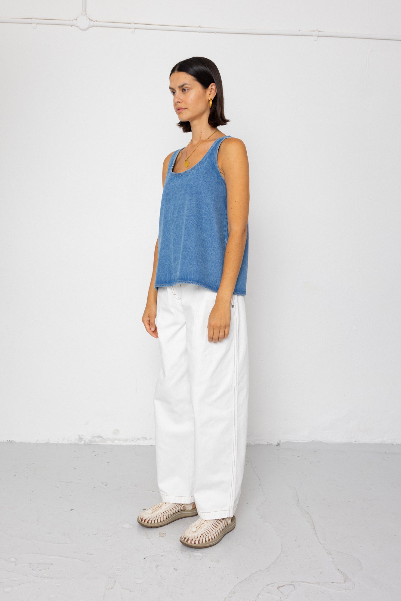 Woman wearing a blue tank top and white pants against a white background