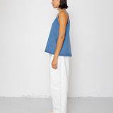 Woman wearing a denim tank top and white pants on a plain background