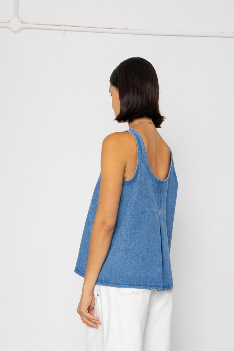 Woman wearing a denim tank top and white pants on a plain background