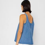 Woman wearing a denim tank top and white pants on a plain background