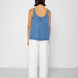 Person wearing a denim tank top and white pants against a white background