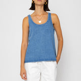 Woman wearing a denim tank top and white pants on a plain background