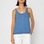 Woman wearing a denim tank top and white pants on a plain background