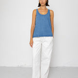 Woman wearing a blue tank top and white pants against a white background