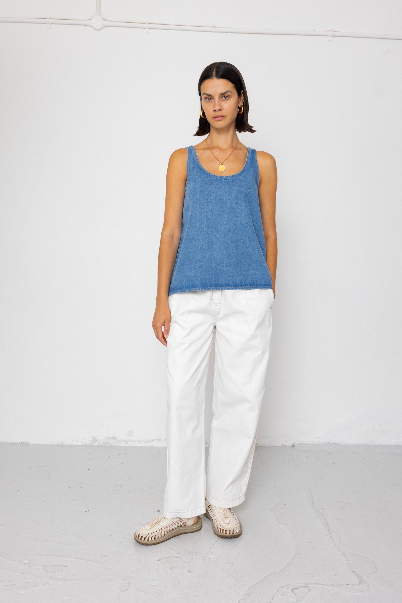 Woman wearing a blue tank top and white pants against a white background