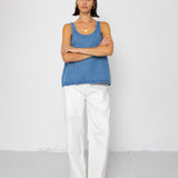 Woman wearing a blue tank top and white pants standing against a white background