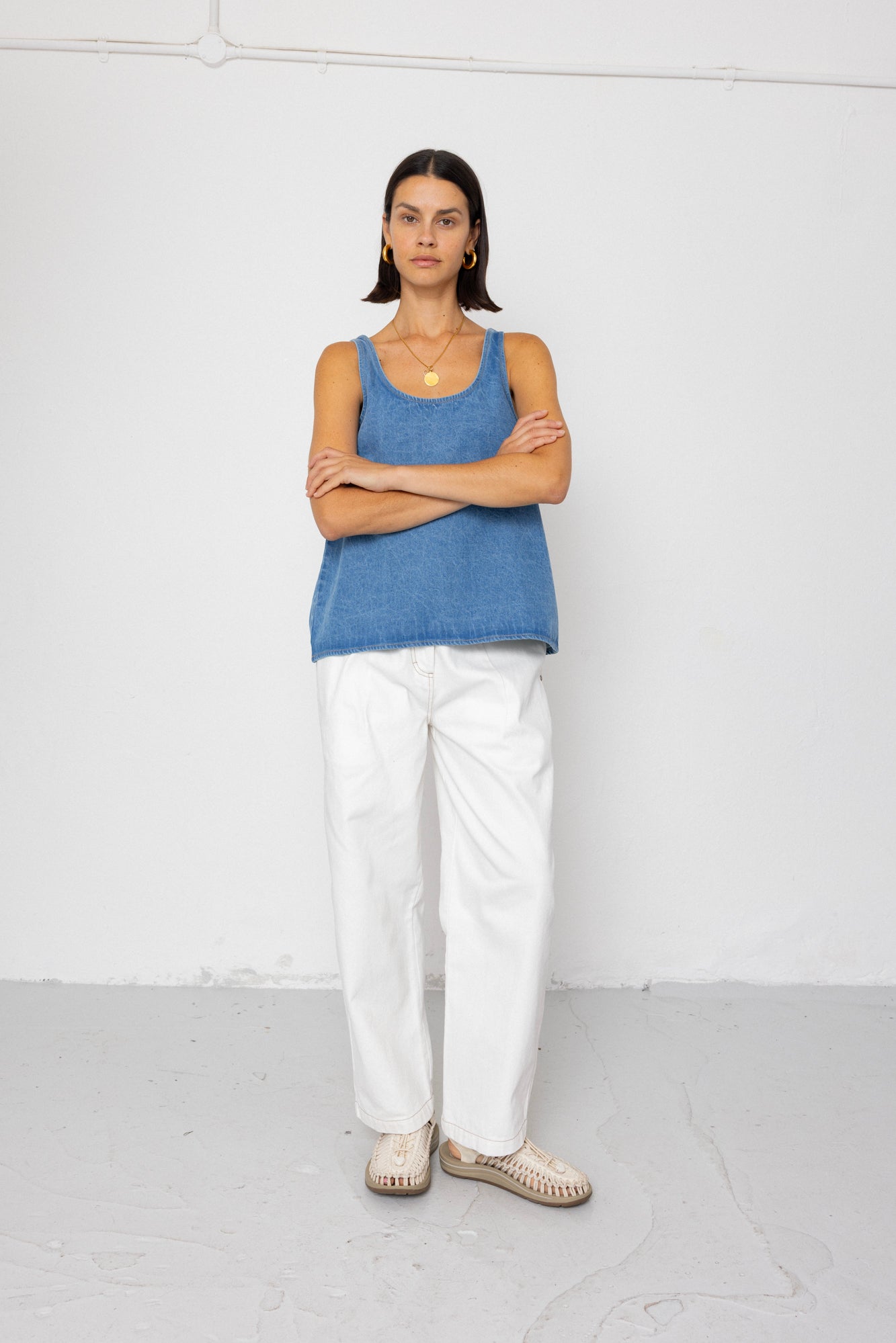 Woman wearing a blue tank top and white pants standing against a white background