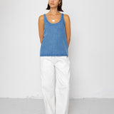 Woman wearing a blue tank top and white pants against a white background