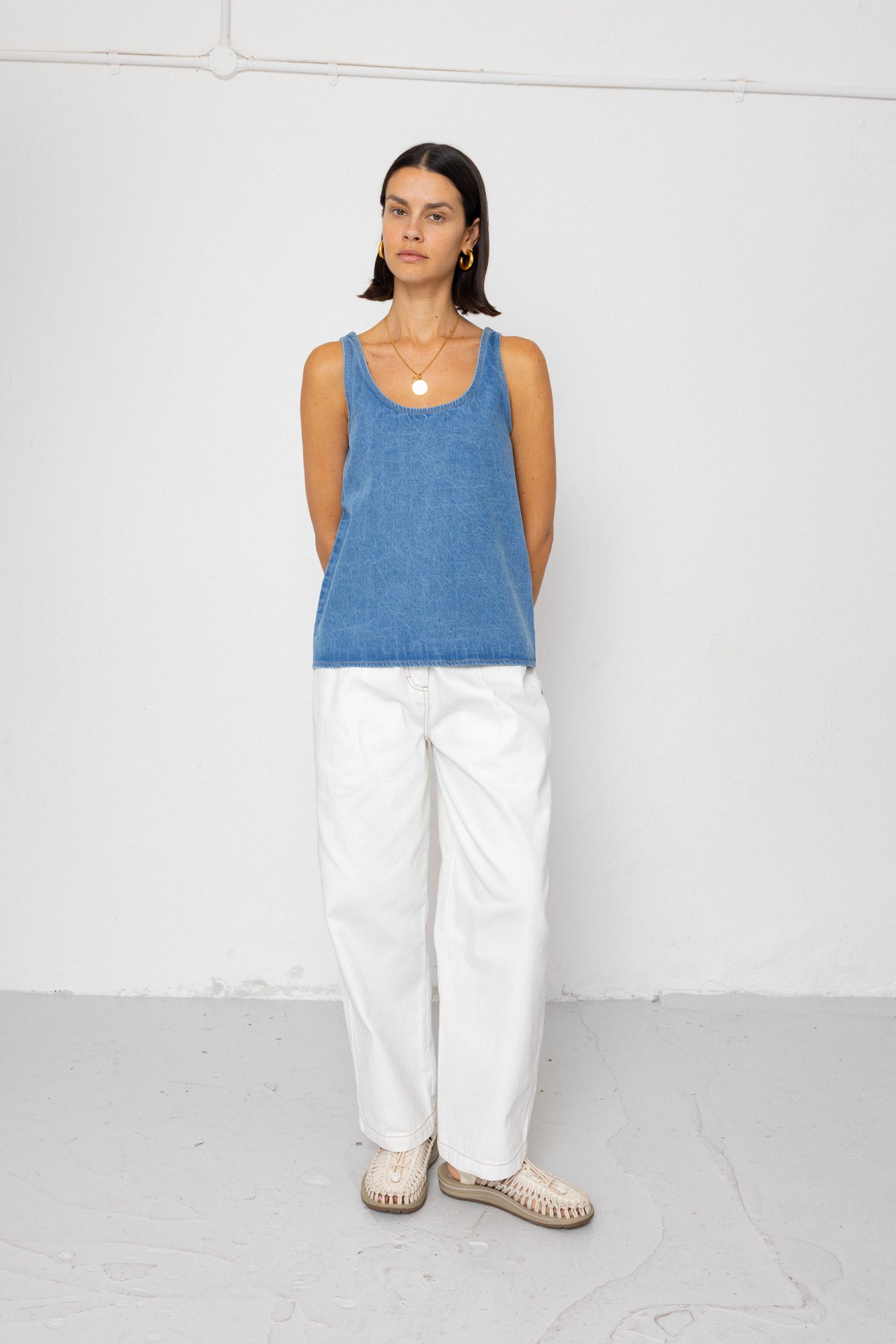 Woman wearing a blue tank top and white pants against a white background