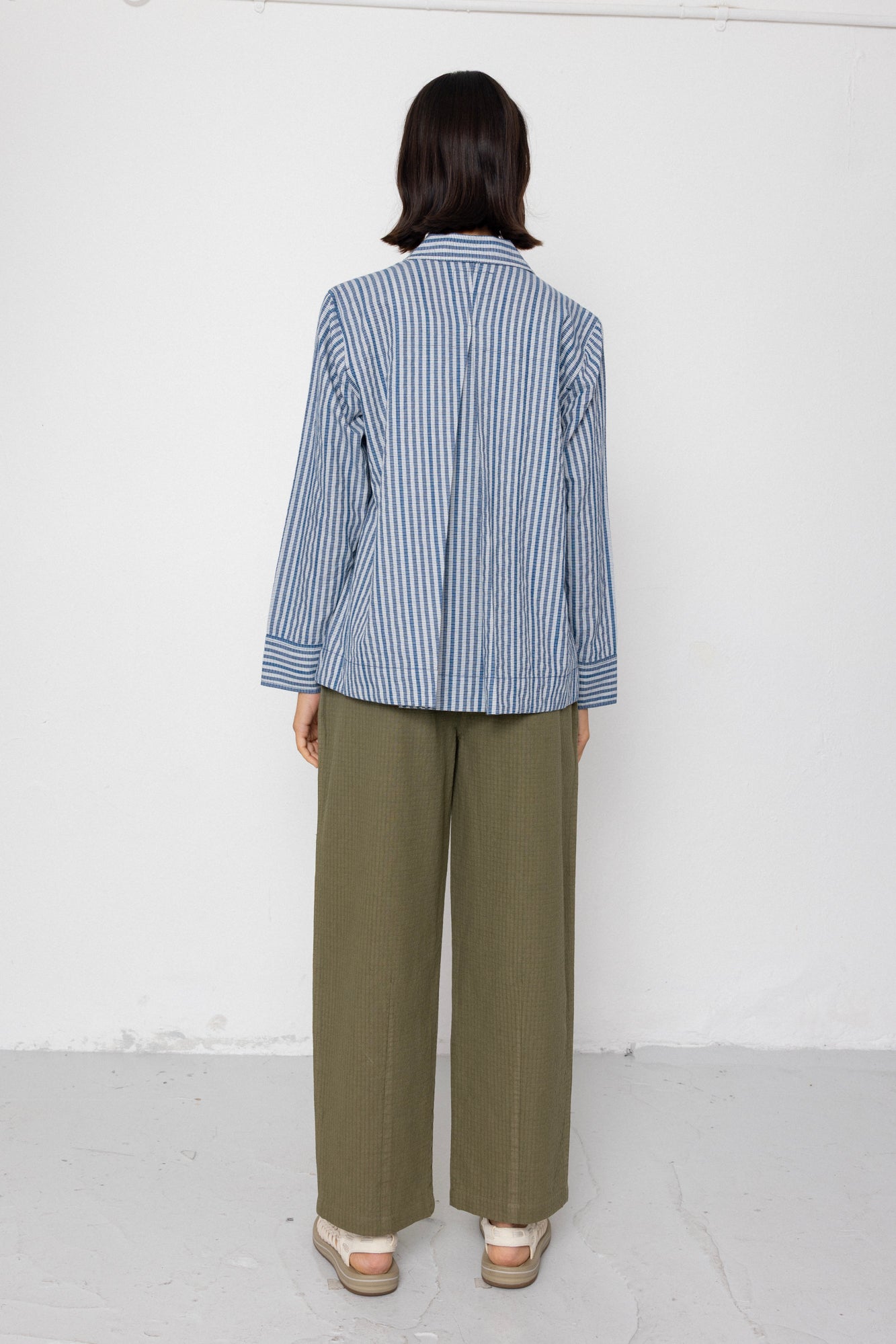 Person wearing a blue and white striped shirt and green pants against a white background