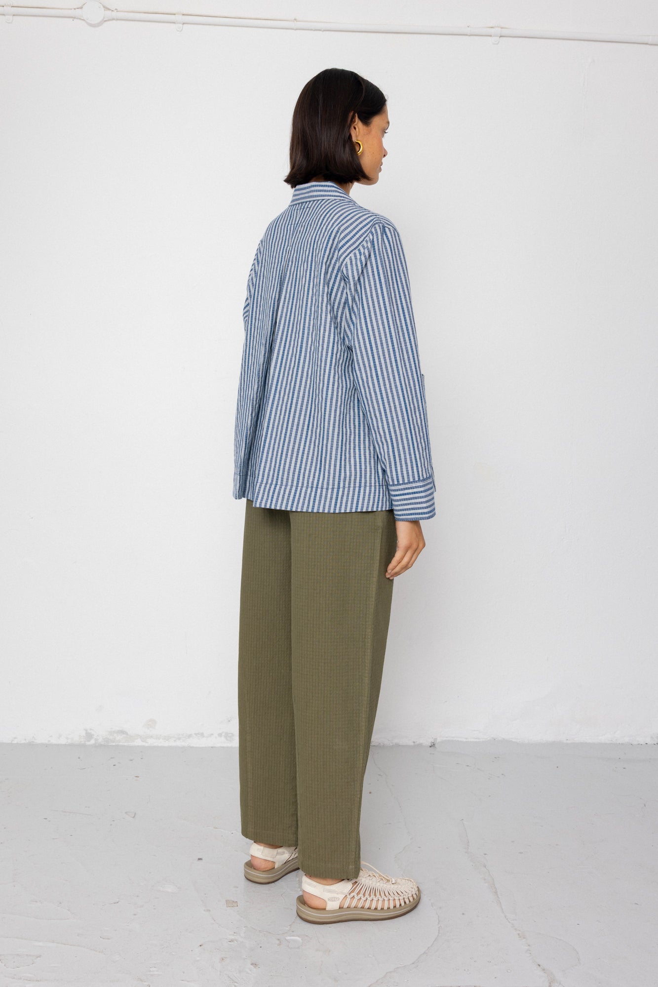Person wearing a blue and white striped shirt and green pants against a white background