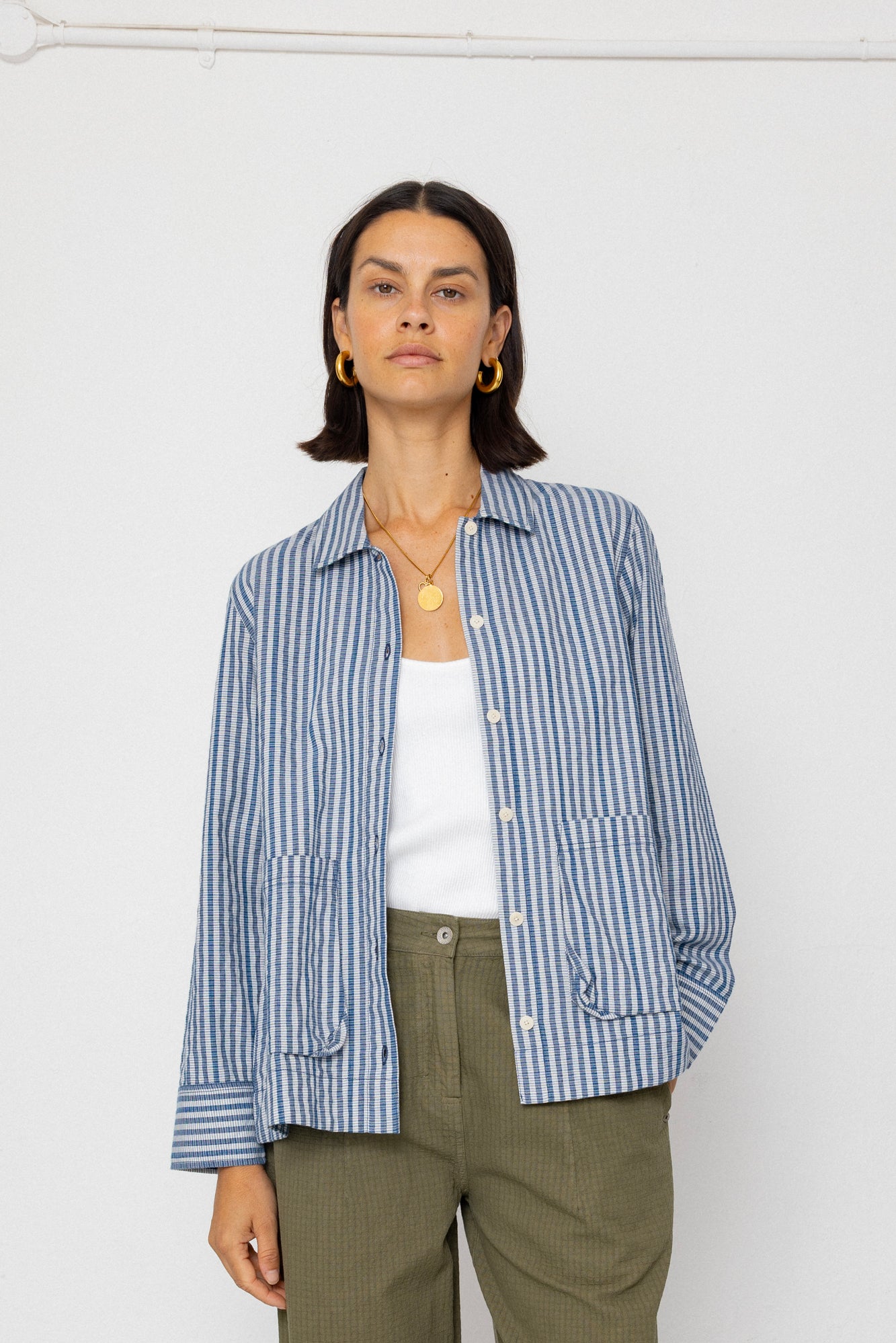 Person wearing a blue striped shirt over a white top and green pants on a white background