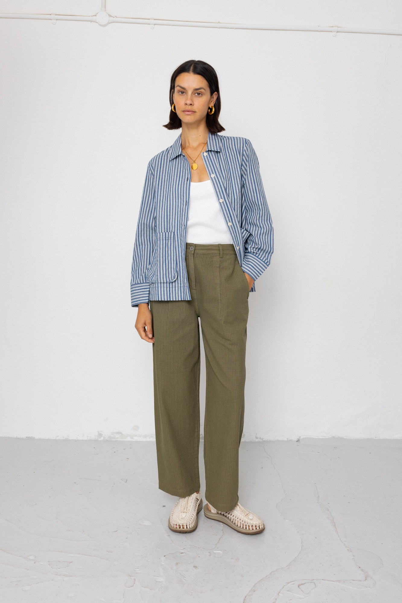 Person wearing a blue striped shirt, white top, green pants, and white shoes on a white background