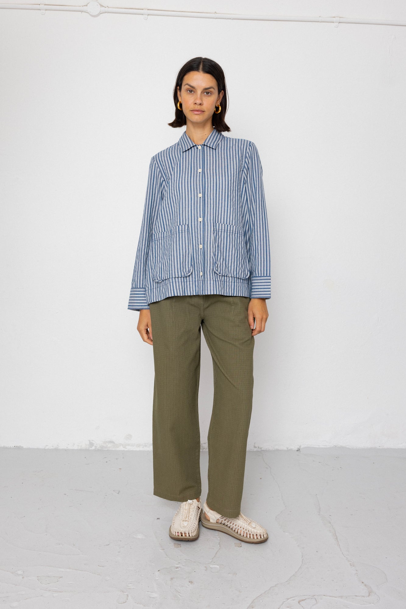 Person wearing a blue striped shirt and green pants against a white background