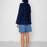 Person wearing a dark blue patterned shirt and denim shorts against a white background