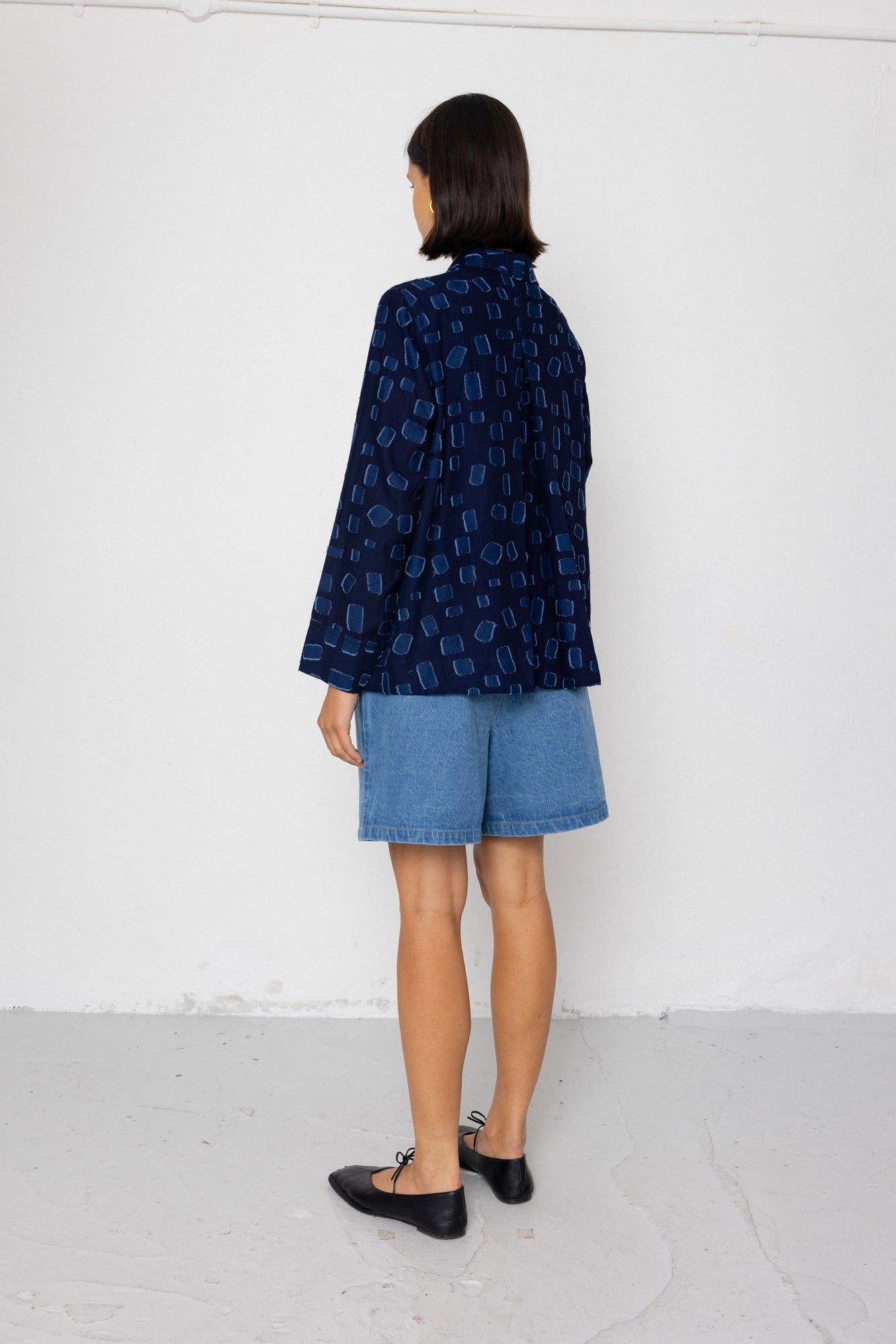 Person wearing a dark blue patterned shirt and denim shorts against a white background