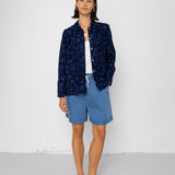 Person wearing a navy patterned shirt over a white top and blue shorts on a light gray background