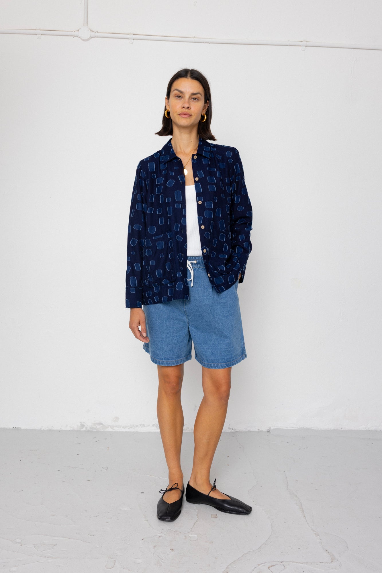 Person wearing a navy patterned shirt over a white top and blue shorts on a light gray background