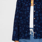 Person wearing a navy patterned shirt over a white top and blue shorts on a light gray background