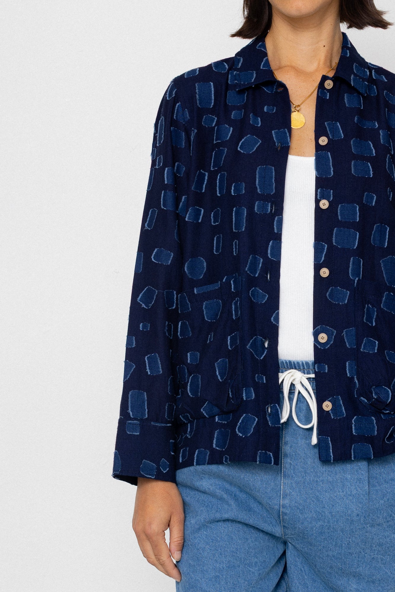 Person wearing a navy patterned shirt over a white top and blue shorts on a light gray background