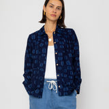 Person wearing a navy patterned shirt over a white top and blue shorts on a light gray background