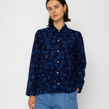 Person wearing a dark blue patterned shirt and denim shorts on a white background