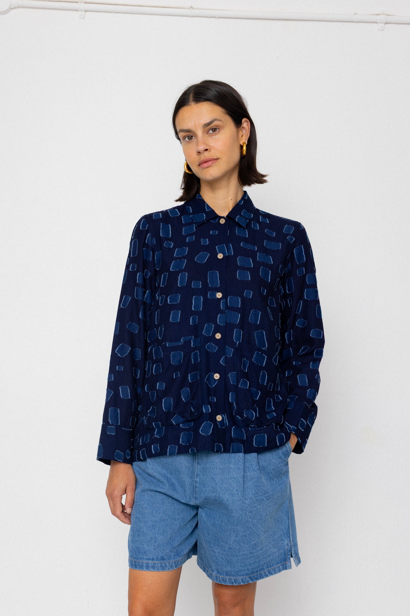 Person wearing a dark blue patterned shirt and denim shorts on a white background