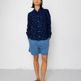 Person wearing a dark blue patterned shirt and light blue shorts against a white background