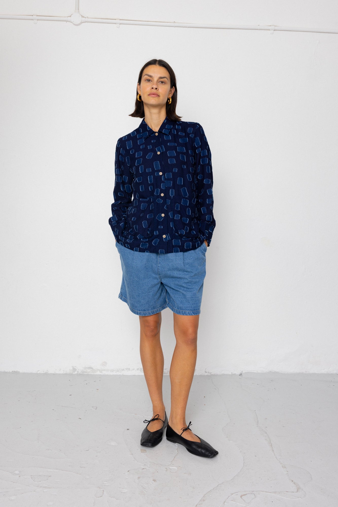 Person wearing a dark blue patterned shirt and light blue shorts against a white background