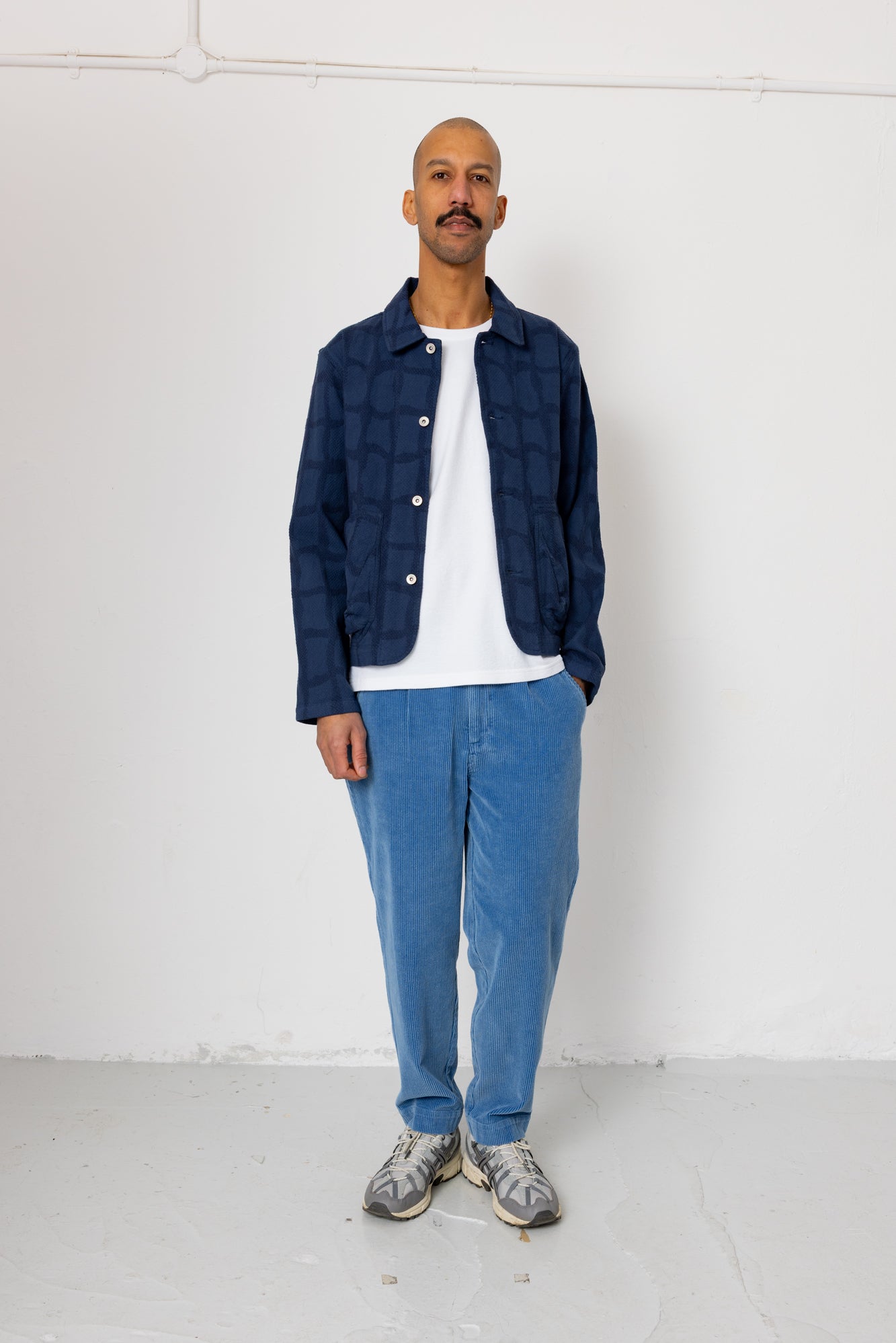 Man wearing a blue jacket, white shirt, and blue jeans standing against a white background