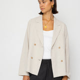 Woman wearing a beige blazer over a white top and black pants on a white background