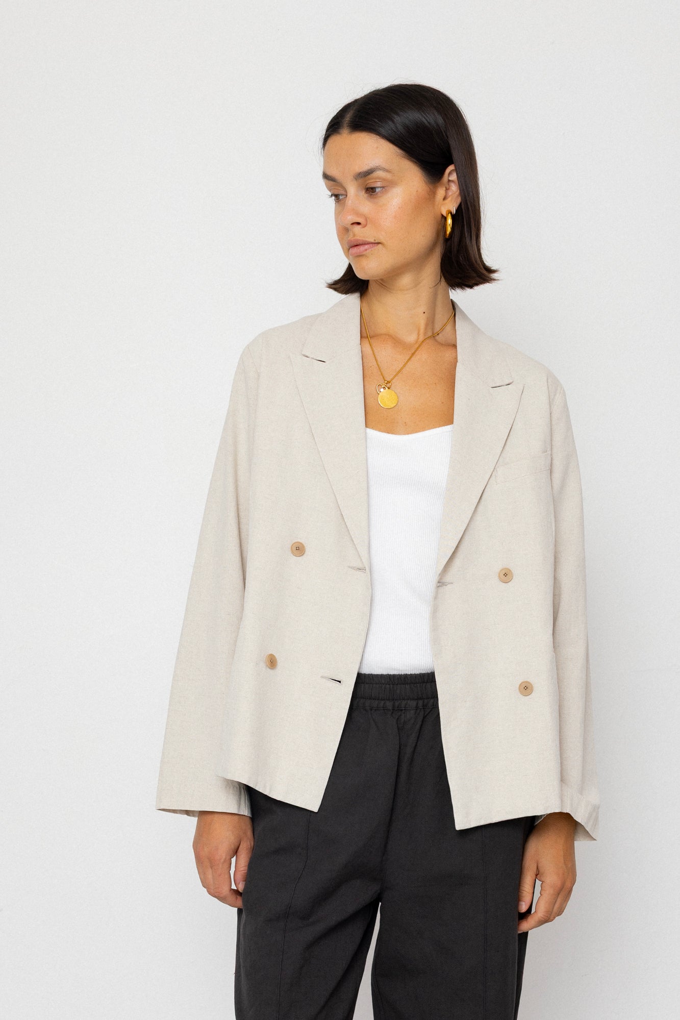 Woman wearing a beige blazer over a white top and black pants on a white background
