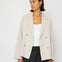 Woman wearing a beige blazer over a white top and black pants on a white background