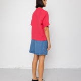 Person wearing a red shirt and blue shorts standing against a white wall.